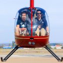 Shot of two people in a red helicopter that is taking off.